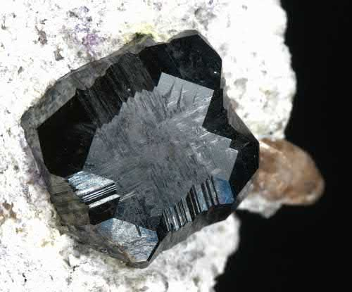 FIGURE 2. Bixbyite, Mn31 2 O3, modified cube about 5 mm crystal, with a topaz, Al2(SiO4)(F,OH)2, crystal in the background.